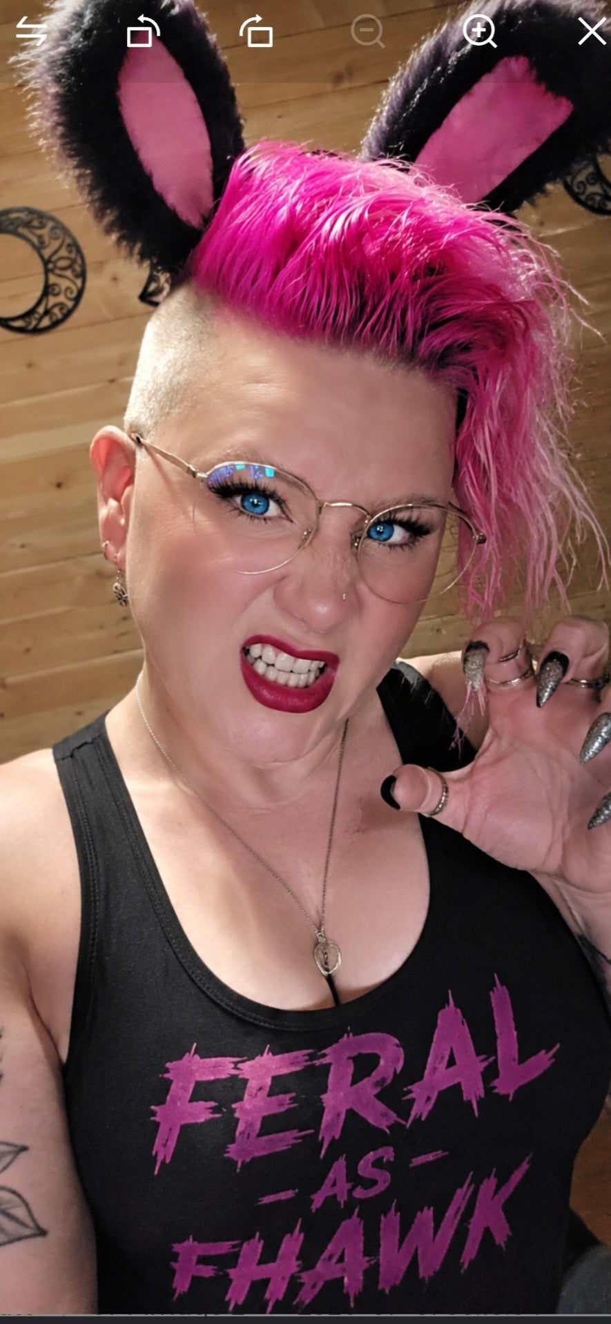Feral as Fhawk™ founder Devon with pink mohawk, black bunny ears, blue eyes, bold red lips and long black claw nails, wearing a black Feral as Fhawk™ tank top. Claws out, unapologetic feral energy. Feral as Fhawk™.