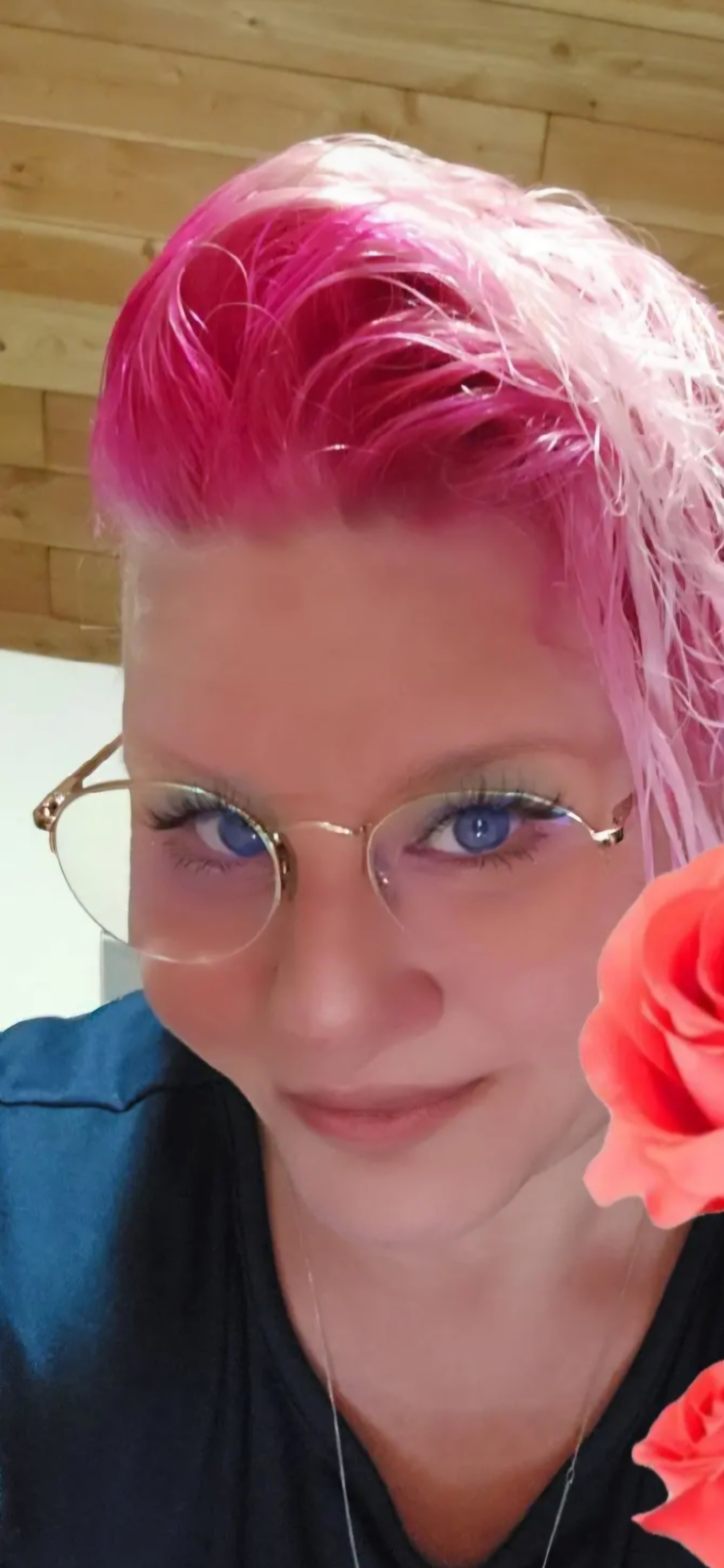 Devon, co - founder of Feral as Fhawk™, with bold pink hair, round glasses, and blue eyes — fierce, feral, and unapologetically themselves.